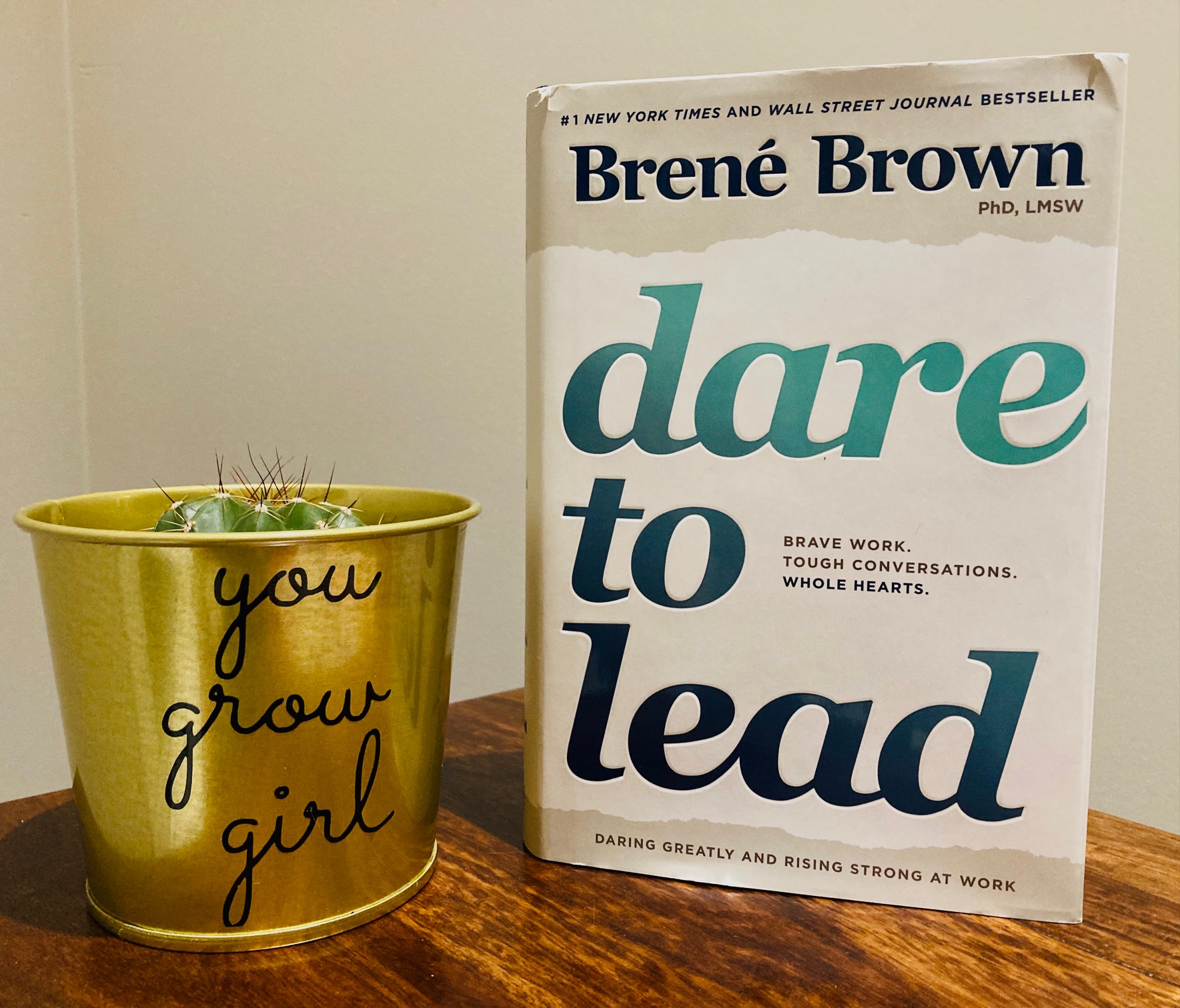 Dare to Lead by Brene Brown book pictured next to a cactus standing on a wooden surface