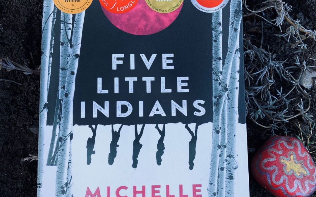 picture of Five Little Indians book by Michelle Good on the ground with a painted rock and dead branches beneath it