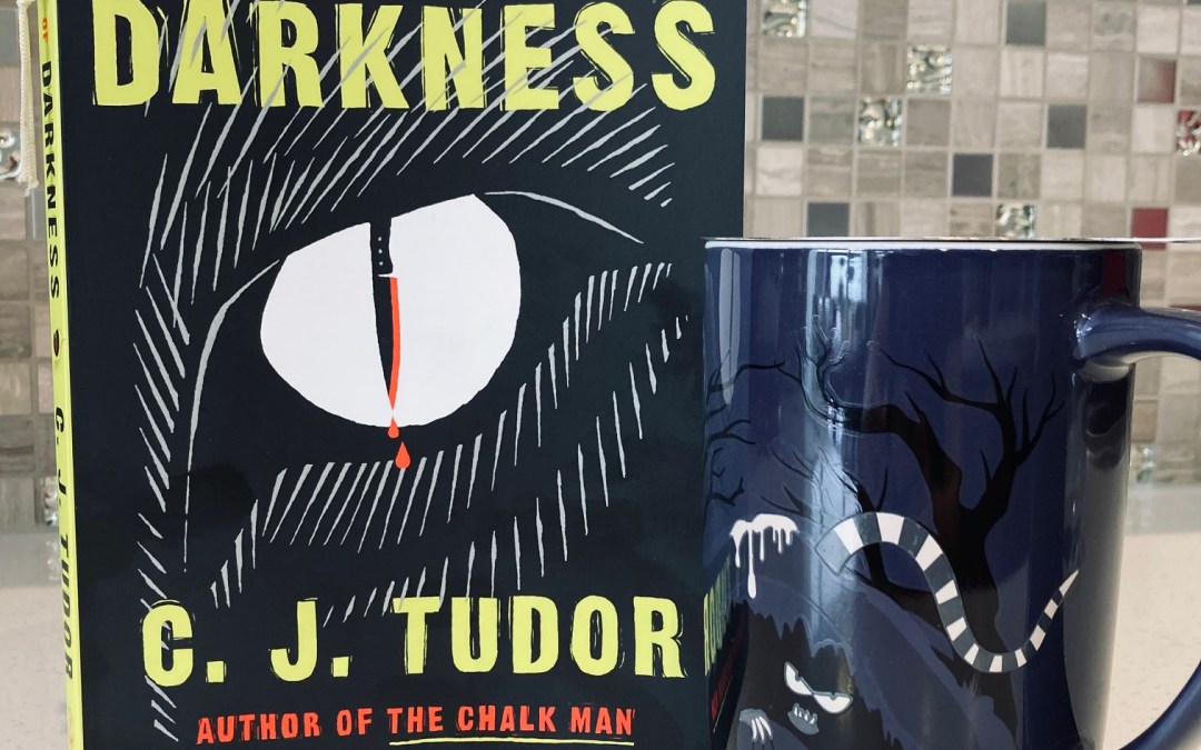A Sliver of Darkness by C.J. Tudor book pictured beside a mug with creepy eyes and a scary looking snake on it