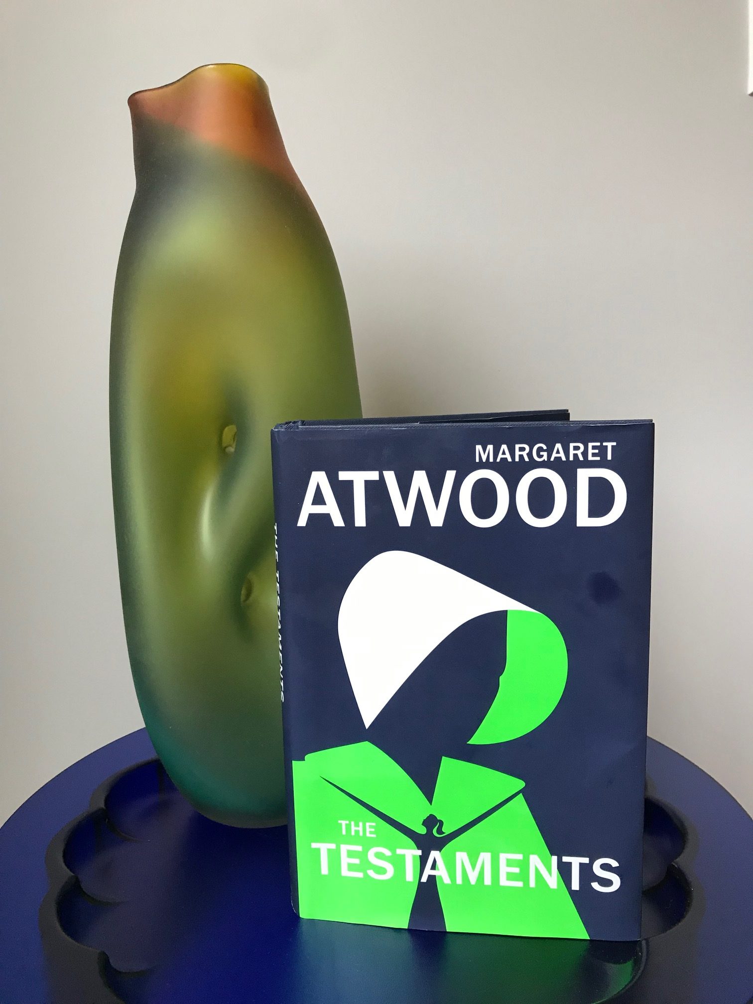 The Testaments by Margaret Atwood book pictured beside a green glass vase