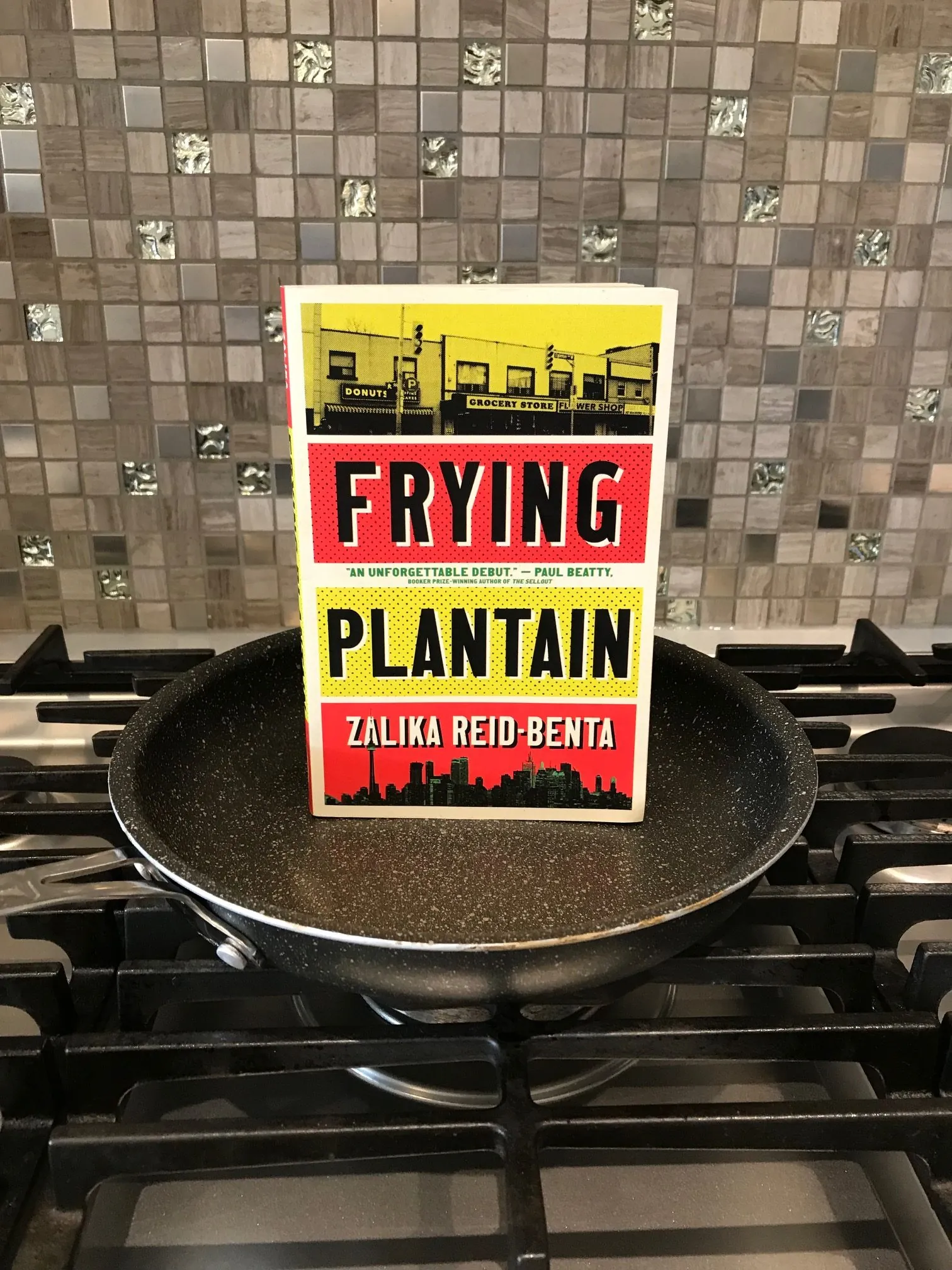 Frying Plantain book by Zalika Reid Benta pictured in a black frying pan sitting on an unlit gas stove
