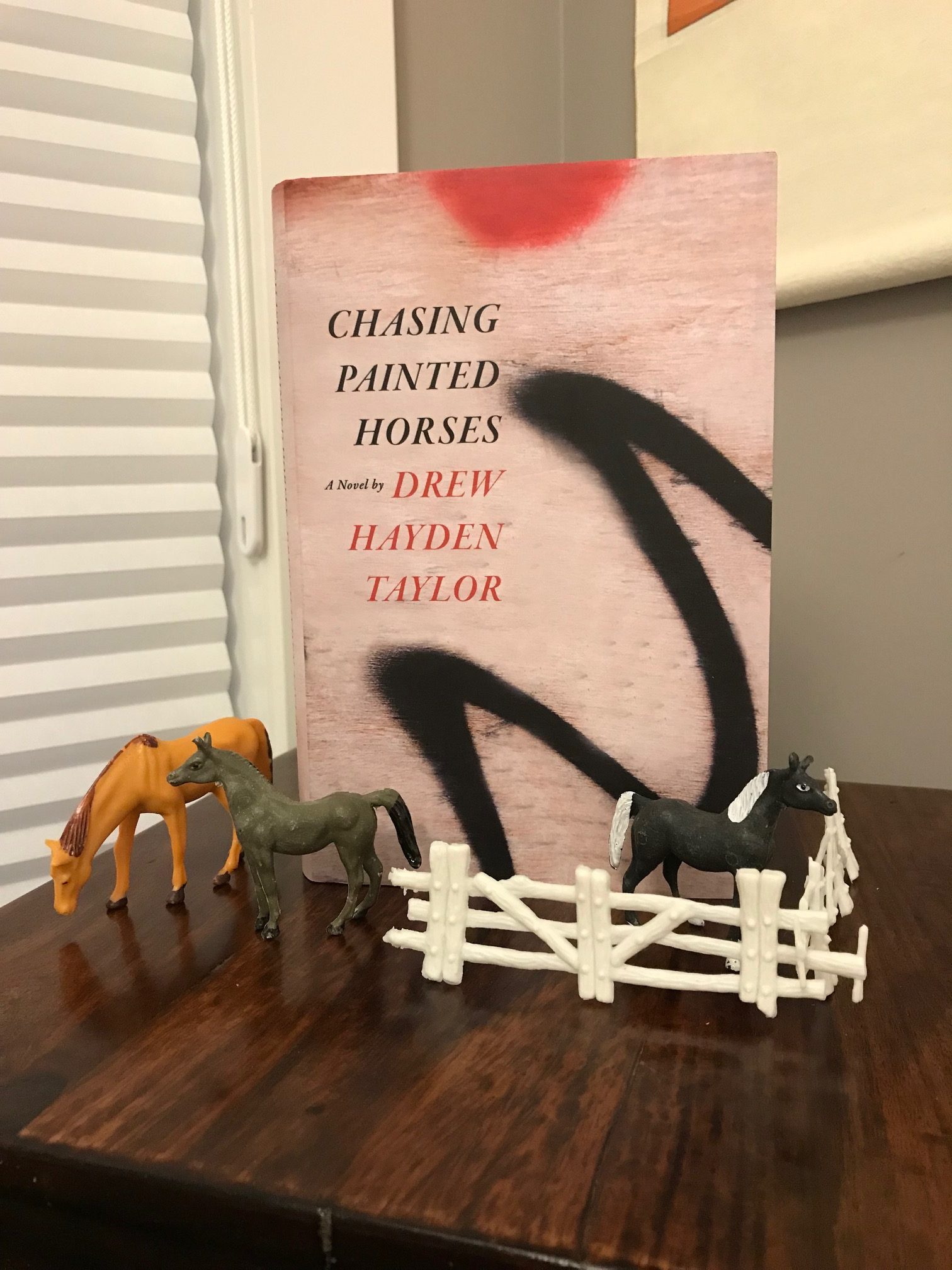 Chasing Painted Horses by Drew Hayden Taylor book, with small plastic horses and a white fence setup around the book