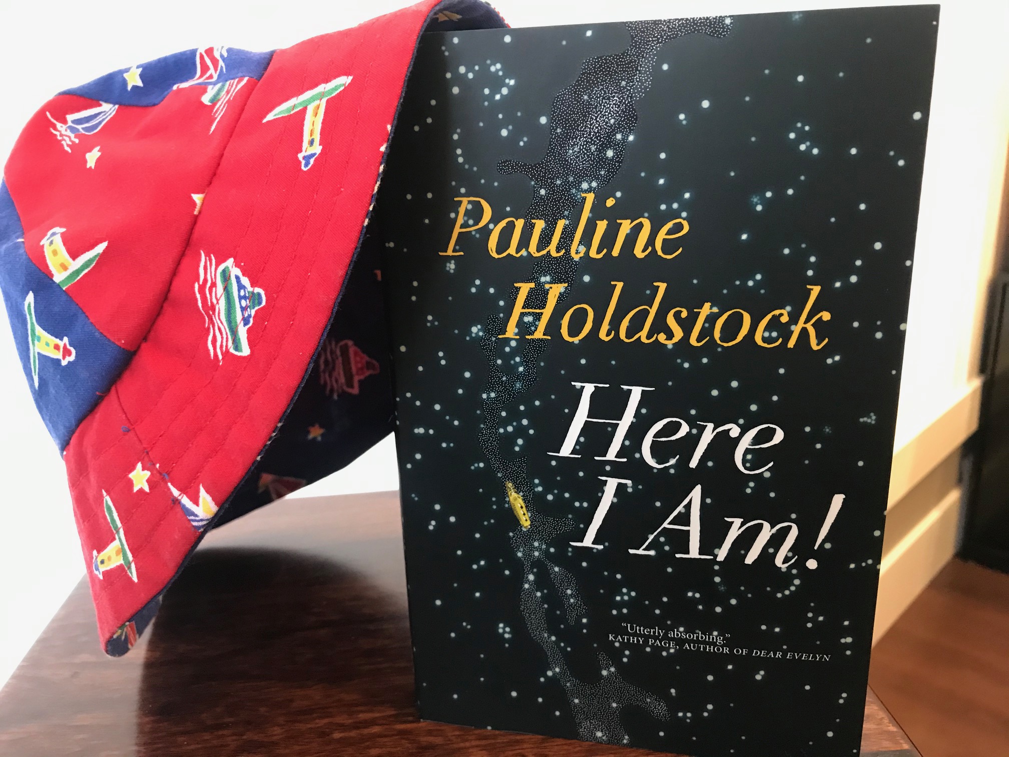 Here I Am! by Pauline Holdstock book with a young boy's blue and red hat sitting against it