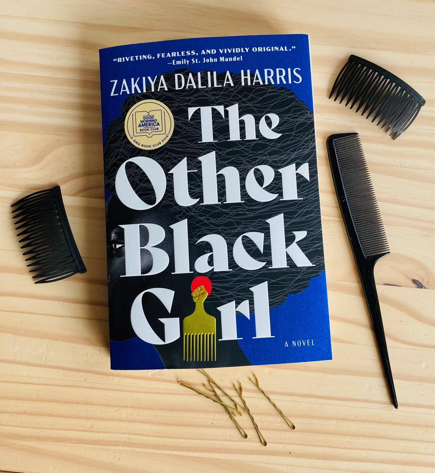 The Other Black Girl by Zakiya Dalila Harris book pictured beside some combs