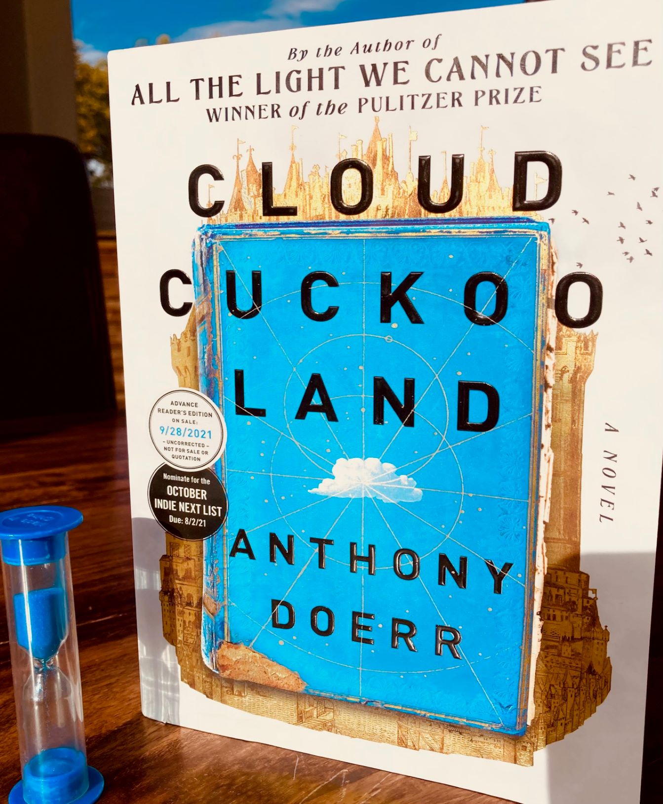 Cloud Cuckoo Land by Anthony Doerr book standing up next to a small hourglass filled with blue sand
