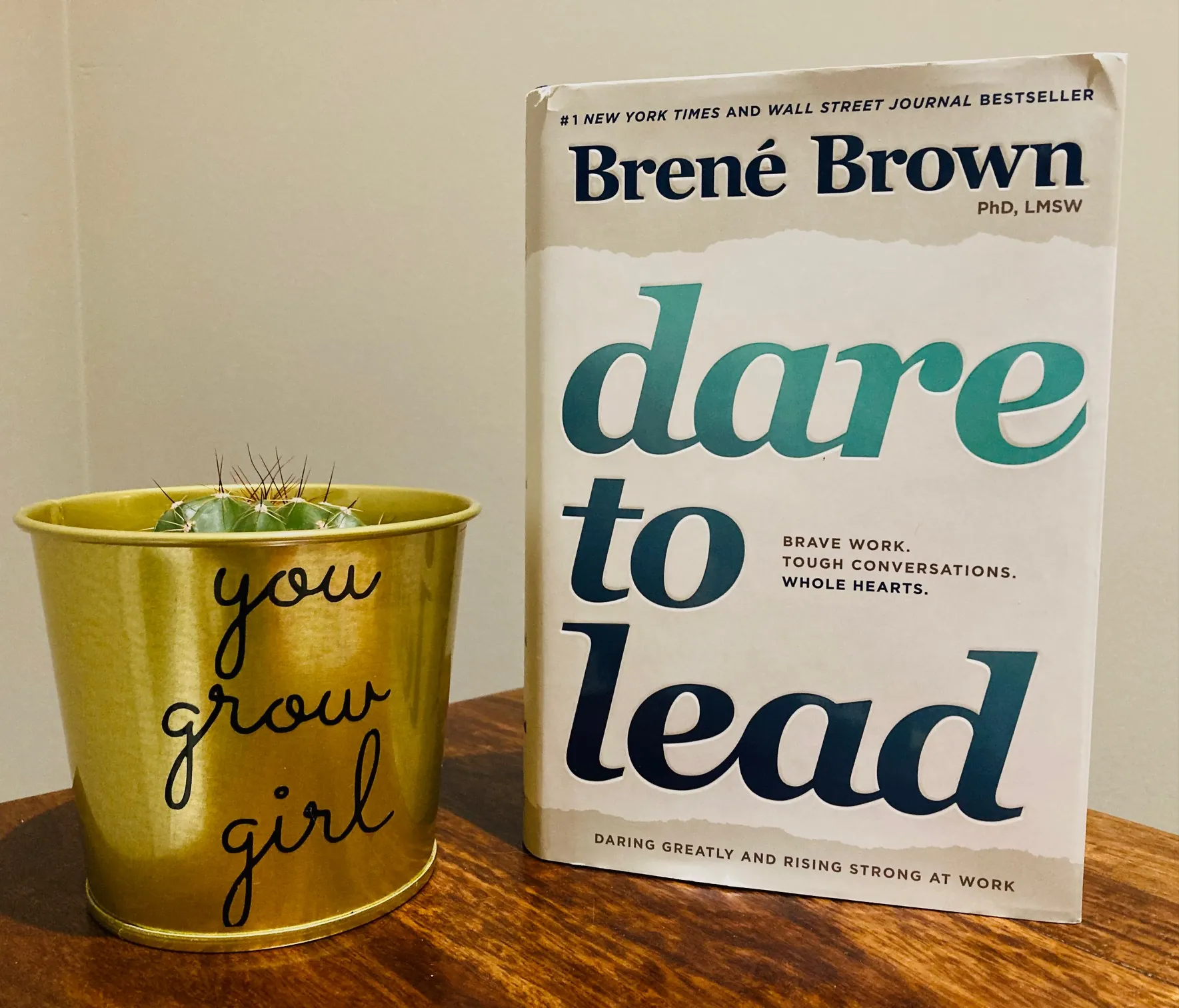 Dare to Lead by Brene Brown book pictured next to a cactus standing on a wooden surface