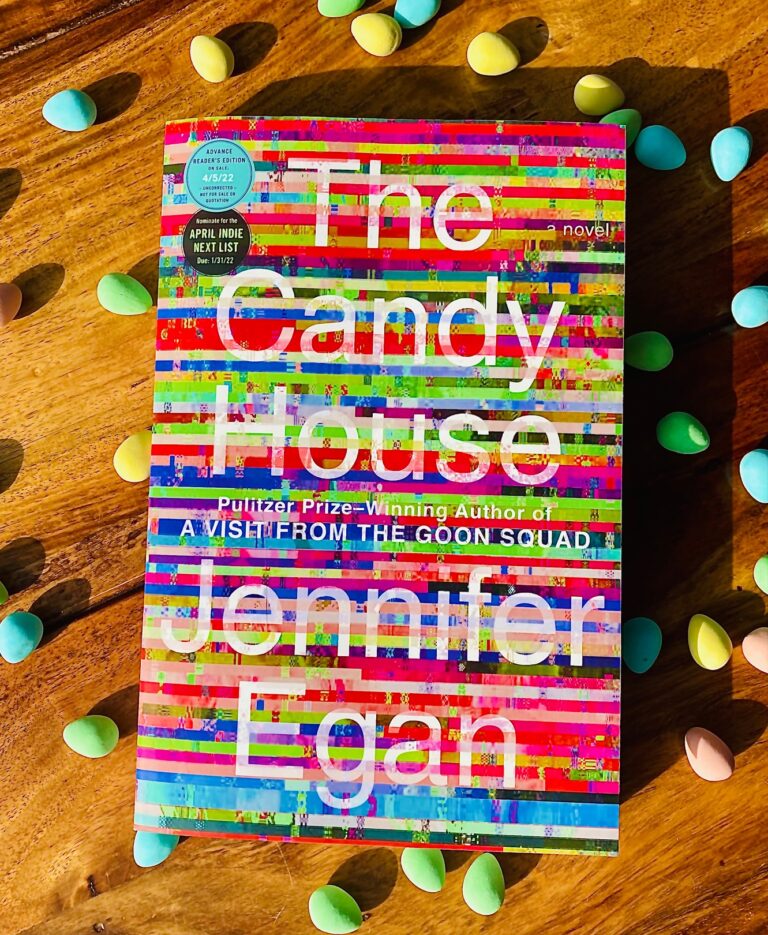 The Candy House by Jennifer Egan book with small multicoloured candies surrounding the book on a wooden background