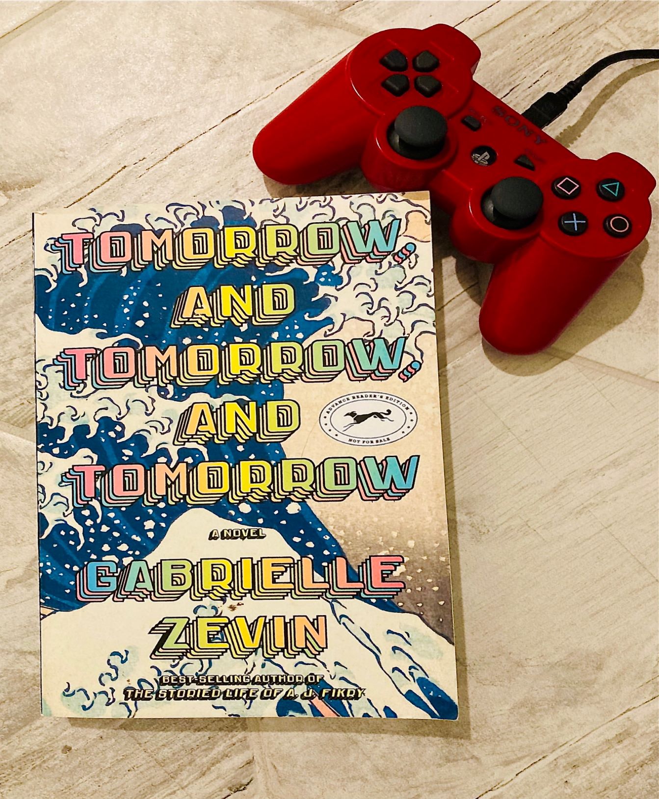 picture of Tomorrow, and Tomorrow, and Tomorrow book by Gabrielle Zevin, on a distressed white background with a red remote control on the top right hand corner