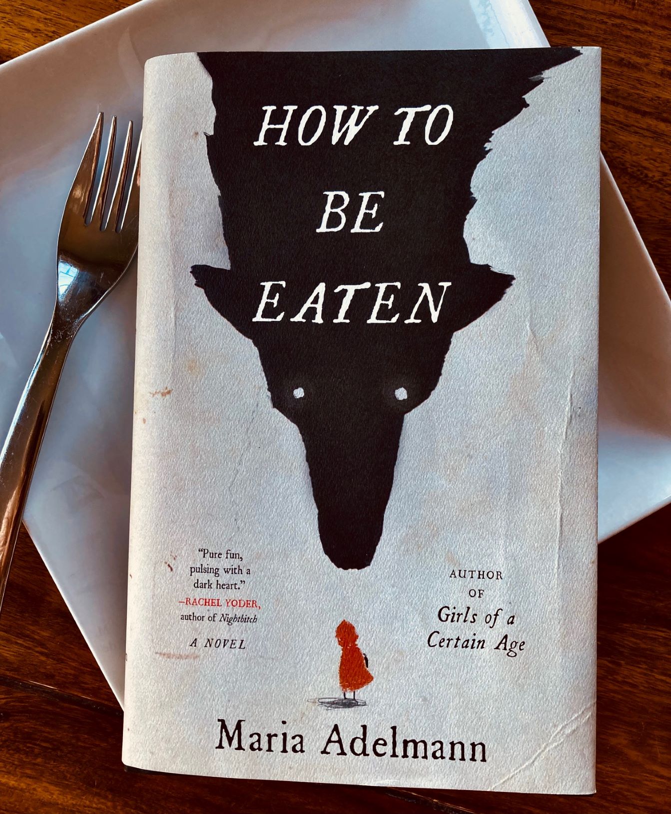 How to Be Eaten by Maria Adelmann book pictured on a dinner plate with a fork on the left hand side of it