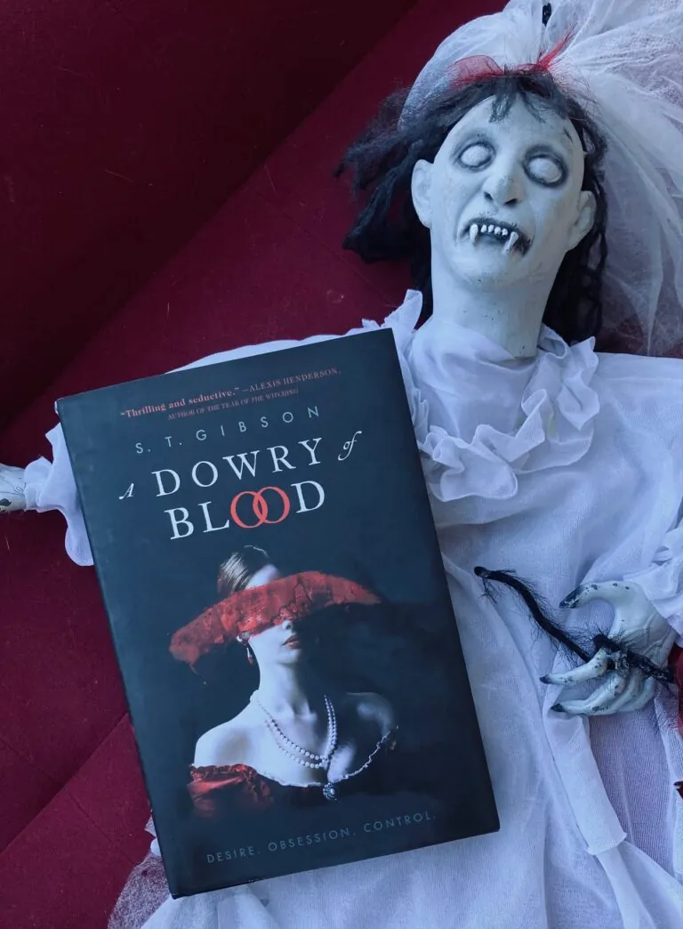 A Dowry of Blood by S.T. Gibson book pictured on top of a creepy white Halloween doll