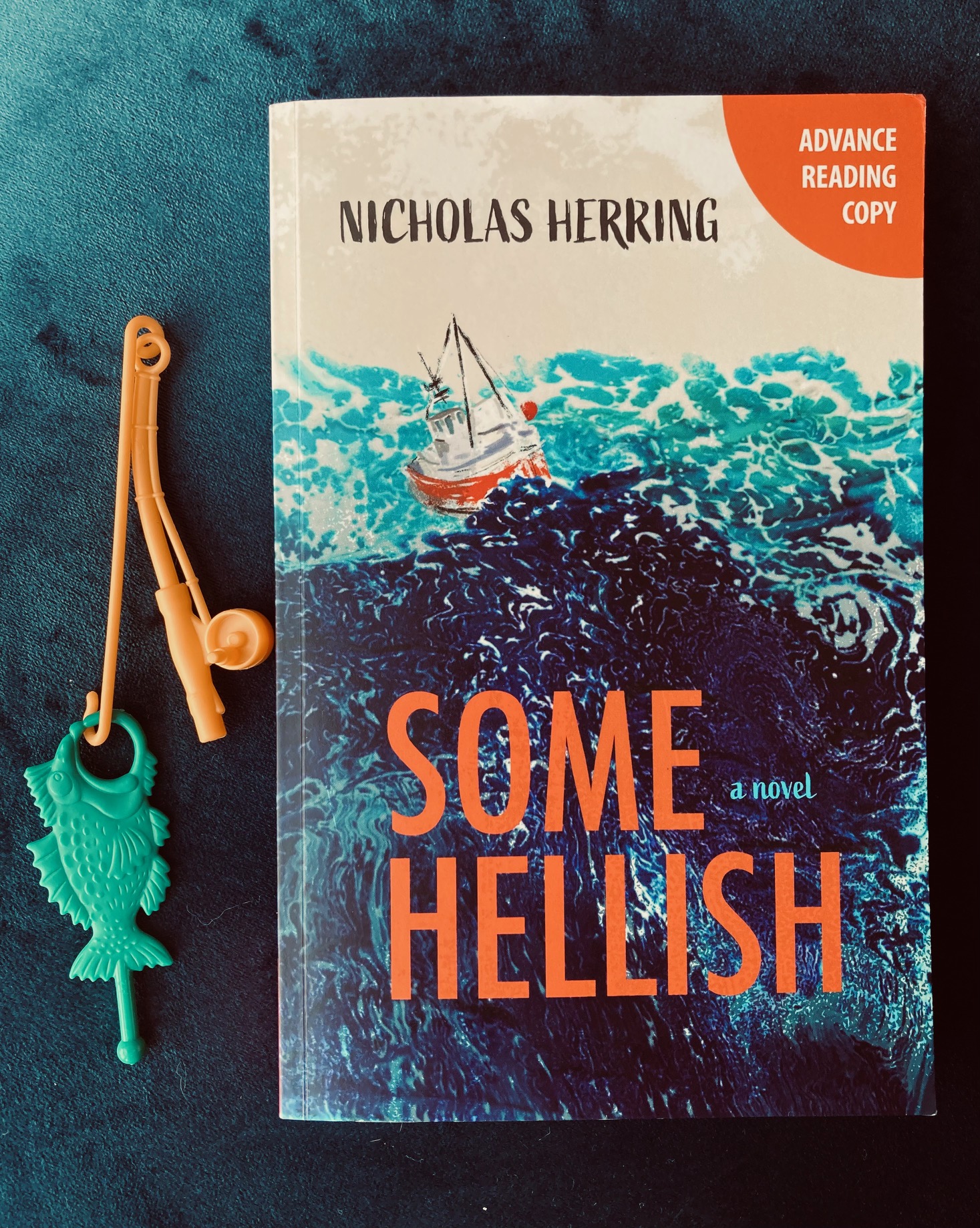 Some Hellish by Nicholas Herring book with a toy fish and fishing pole next to the book