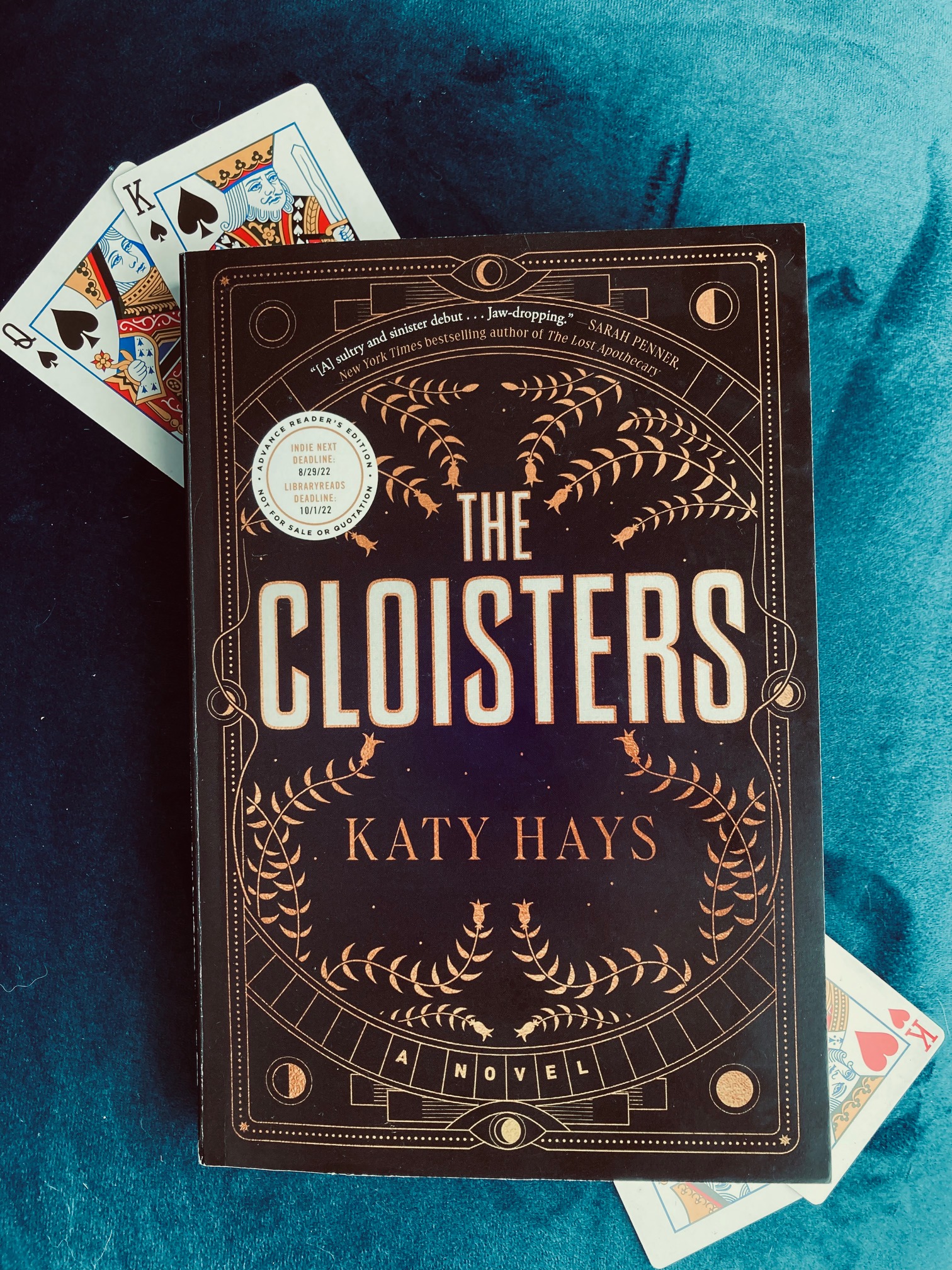 Picture of The Cloisters by Katy Hays book, on a navy blue background with four playing cards arranged behind the book