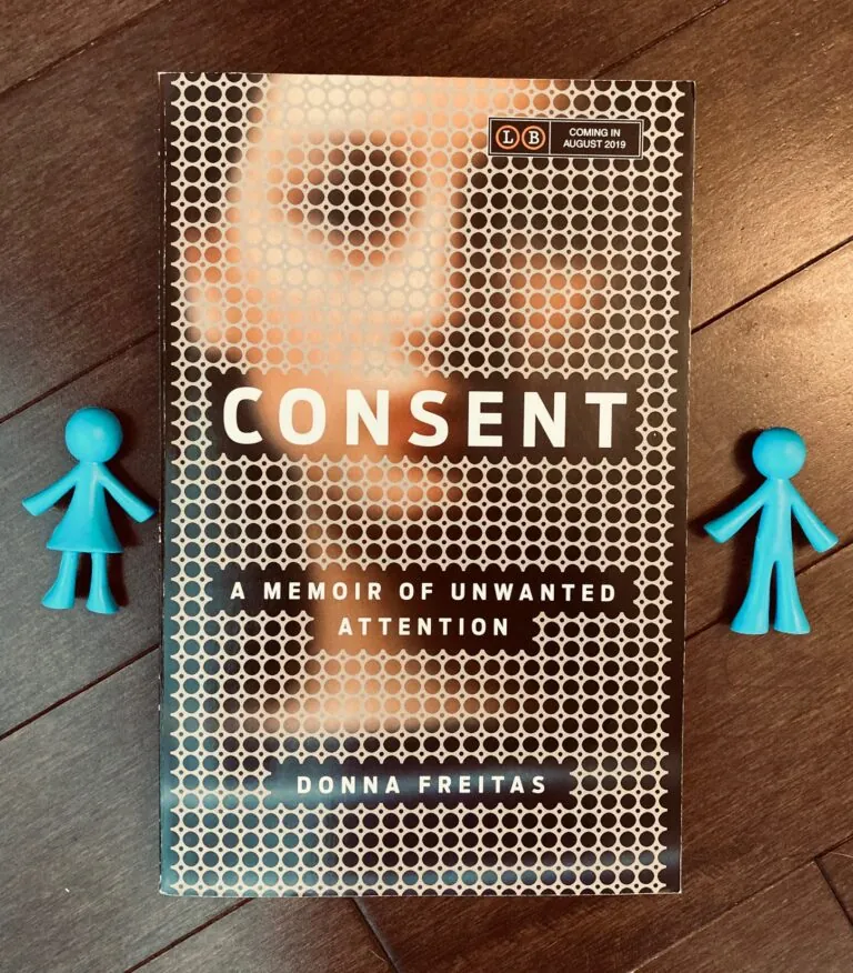 Consent by Donna Freitas book with a blue plastic girl and boy figure on either side of the book, lying on top of a wooden background