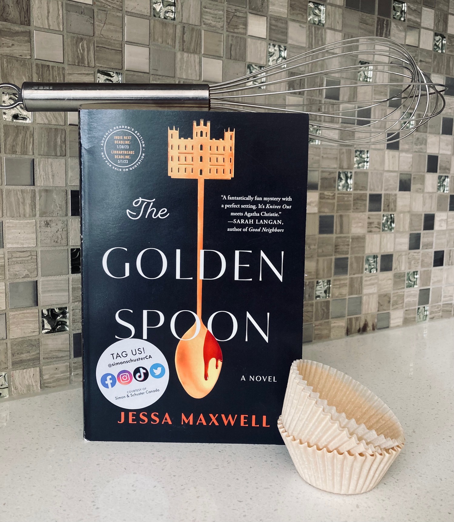 The Golden Spoon by Jessa Maxwell book pictured with paper cupcake liners next to it and a silver whisk on top on a white countertop