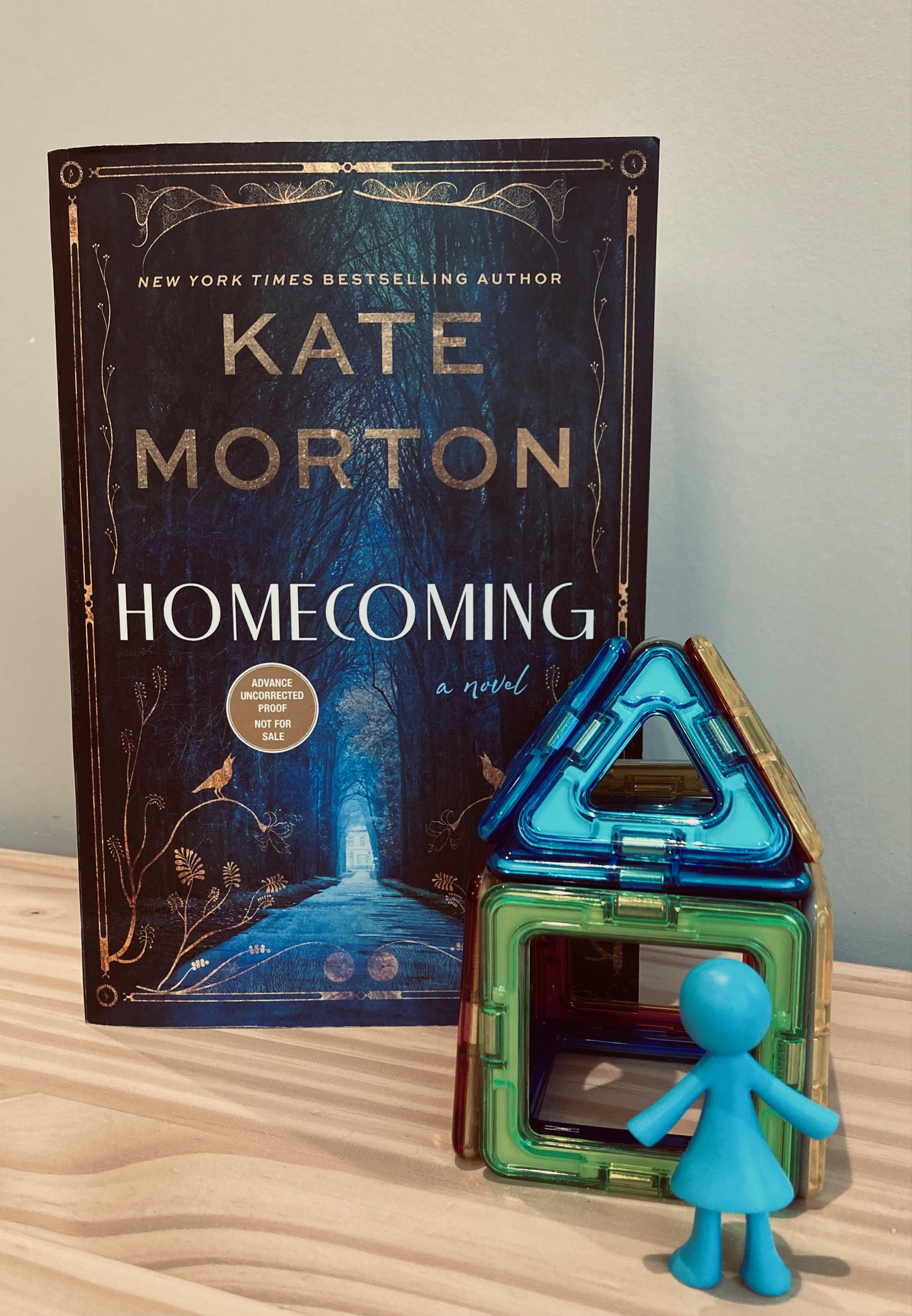 Homecoming by Kate Morton book, standing up beside a small toy house and plastic girl figurine