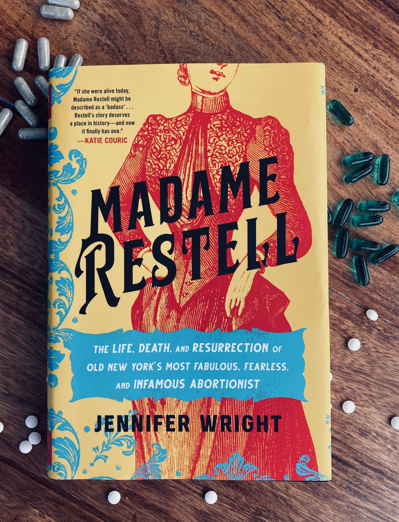 Madame Restell by Jennifer Wright book pictured with scattered pills around it on a brown wooden background