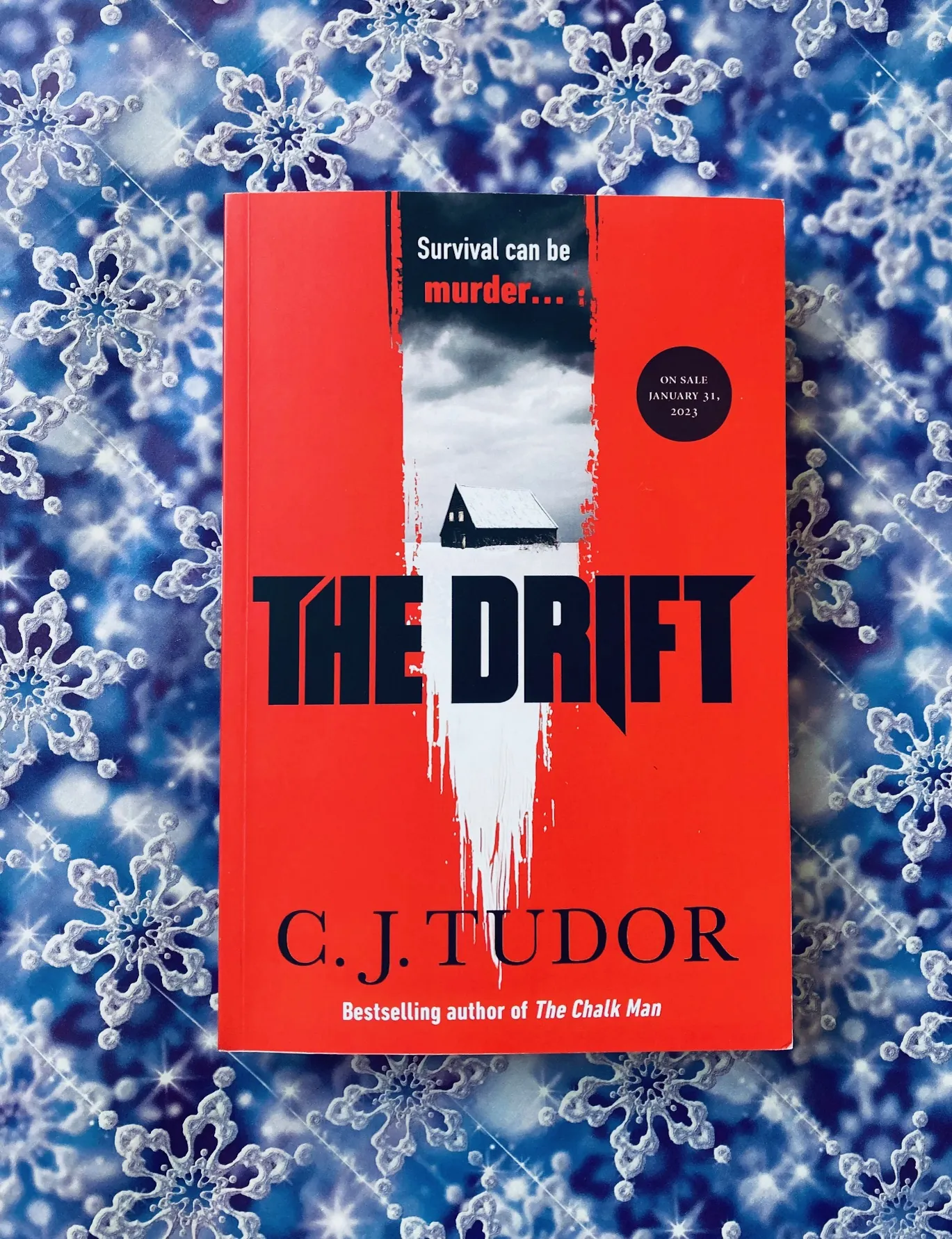 The Drift by C.J. Tudor book pictured on a blue background with snowflakes