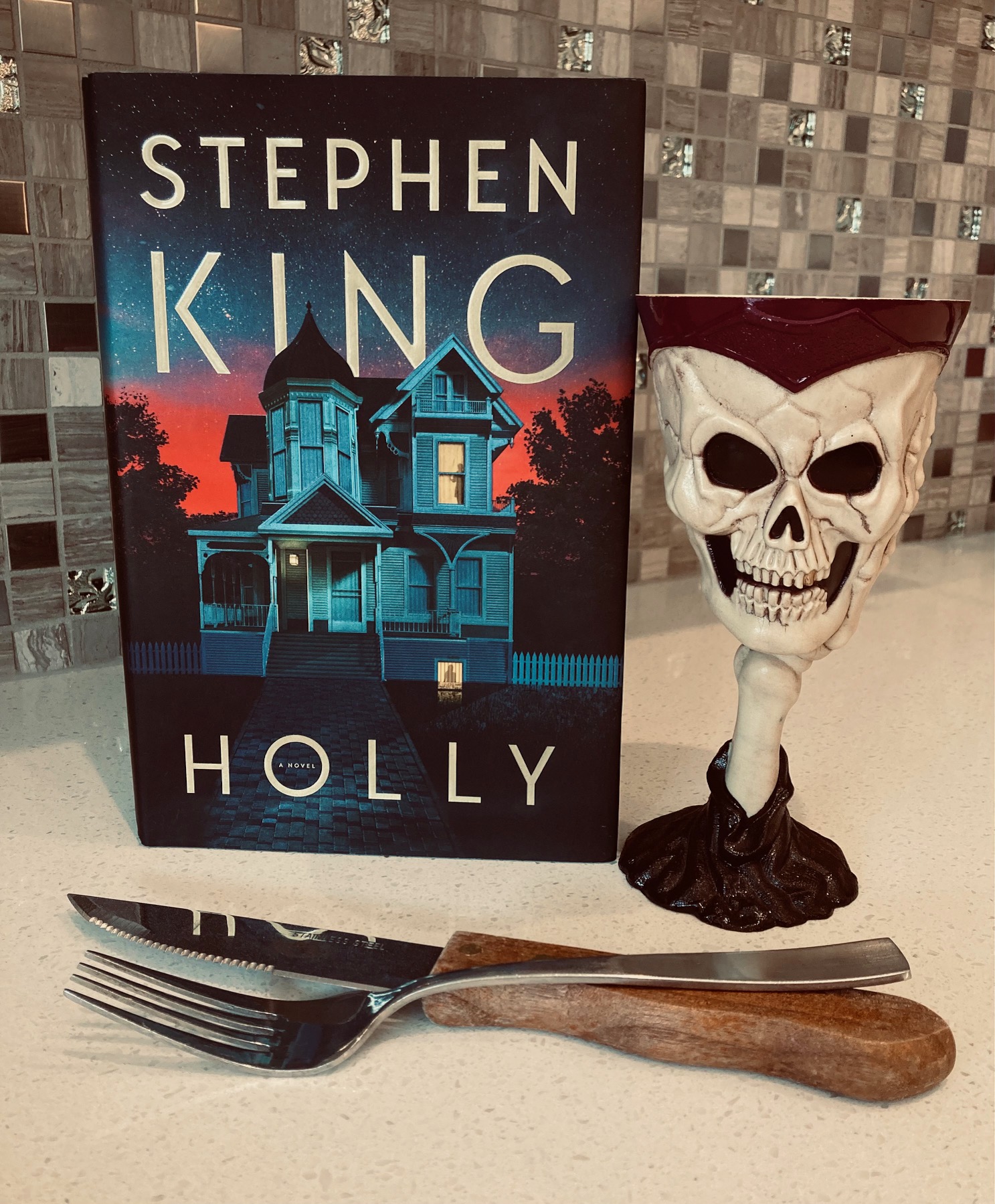 Holly by Stephen King book pictured beside a skull cup and knife and fork