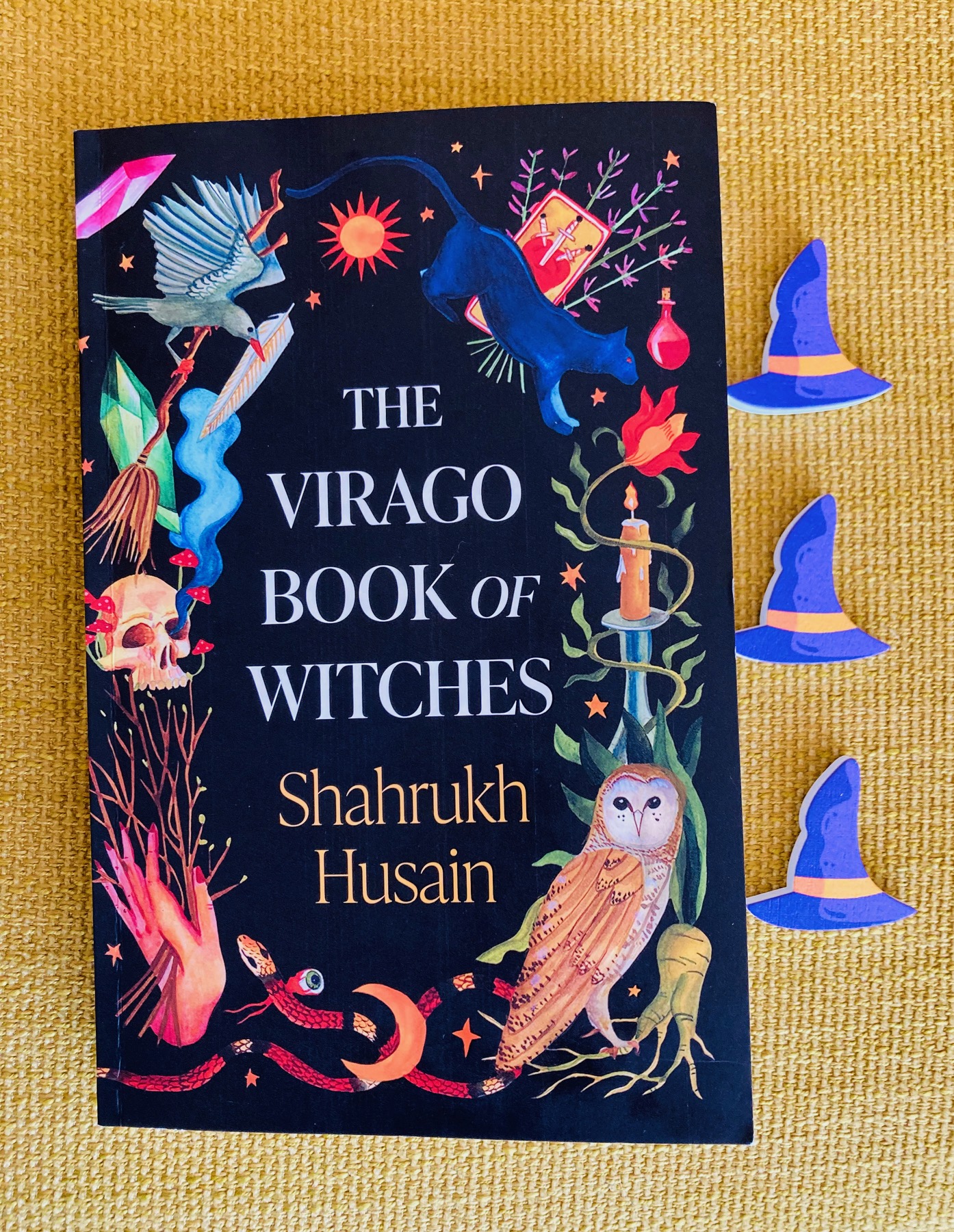 The Virago Book of Witches by Shahrukh Husain pictured beside three small witch hats