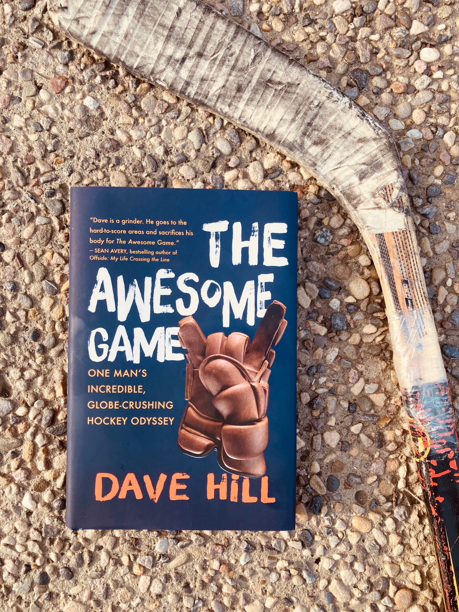 The Awesome Game by Dave Hill book pictured beside a taped up hockey stick